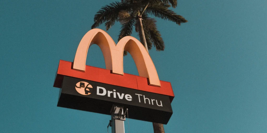 A classic McDonald's pole sign with the iconic golden arches, standing outside a modernized restaurant using AI and edge computing for faster service.